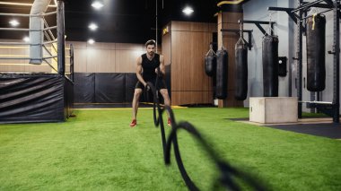 full length of bearded sportsman training with battle ropes