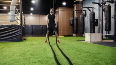 full length of bearded man working out with battle ropes