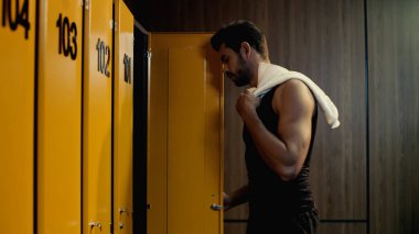 side view of bearded sportsman taking towel in locker room