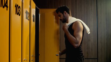 side view of bearded sportsman taking towel in locker room clipart