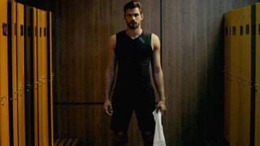 bearded sportsman standing with towel in locker room