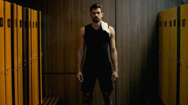 bearded sportsman standing with white towel in locker room