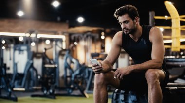 bearded sportsman using smartphone while sitting on car tire 