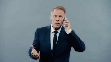 Mature businessman talking on smartphone and looking at camera isolated on grey 
