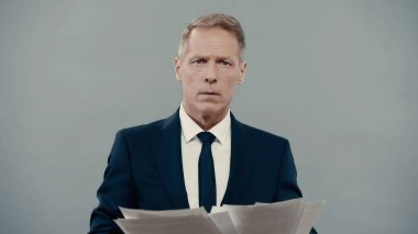 Mature businessman holding papers and looking at camera isolated on grey 