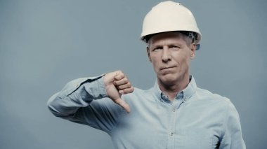 Middle aged engineer in hardhat showing dislike sign isolated on grey 