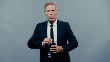 Middle aged businessman holding drinking flask and looking at camera isolated on grey 