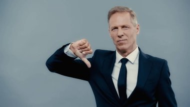 Displeased businessman showing thumb down isolated on grey 