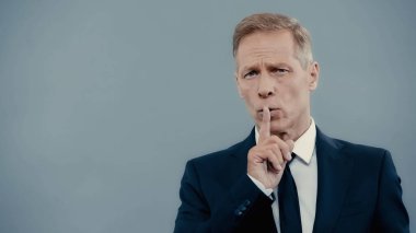 Mature businessman showing secret gesture isolated on grey 