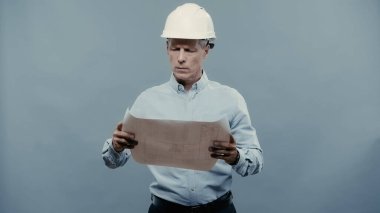 Mature engineer looking at blueprint isolated on grey 