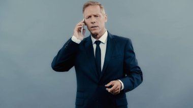 Stressed businessman talking on cellphone isolated on grey 