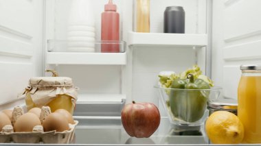 fresh fruits and vegetables near eggs, orange juice and bottles with sauces in fridge