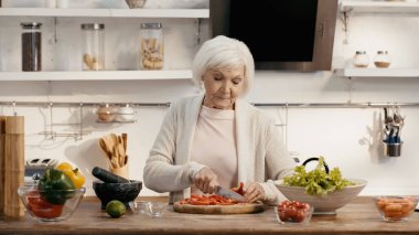 elderly woman preparing thanksgiving dinner and cutting bell pepper in kitchen