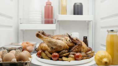 roasted turkey with potatoes and cherry tomatoes near orange juice, carrots and lemon and sauces in fridge