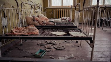 abandoned kindergarten with metal beds, dirty pillows, papers and broken doll in chernobyl 