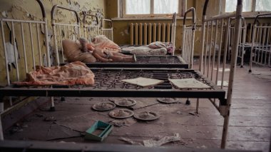 abandoned kindergarten with metal beds, dirty pillows, papers and broken doll in chernobyl  clipart