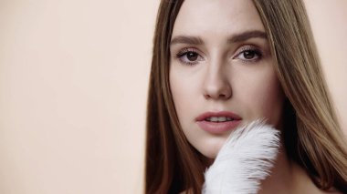 sensual young woman near soft feather isolated on beige 