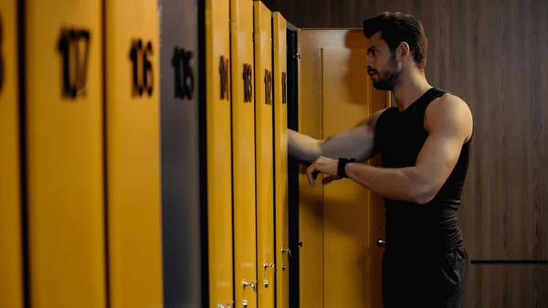 bearded sportsman with smart watch standing in locker room