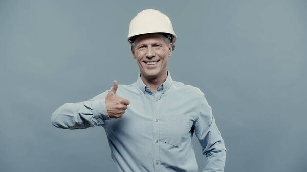 Smiling engineer in hardhat showing like isolated on grey 
