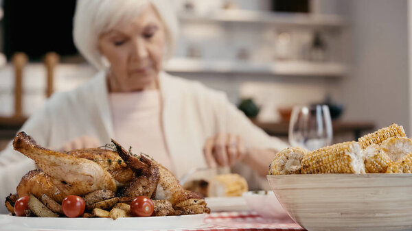 traditional roasted turkey with potatoes and cherry tomatoes near grilled corn and blurred senior woman 