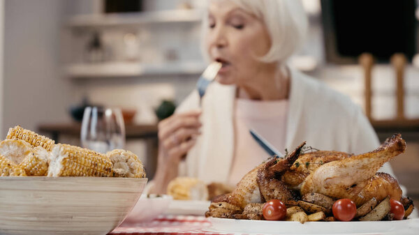 selective focus of roasted turkey and grilled corn near blurred senior woman having thanksgiving dinner
