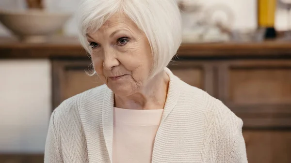 老年妇女 灰白的头发 在模糊的厨房里朝外看 — 图库照片