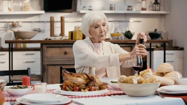 老妇人在烤火鸡 烤玉米和面包附近打开瓶装红葡萄酒 — 图库照片
