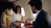 Businesswoman taking glass of champagne near blurred boyfriend in private plane 