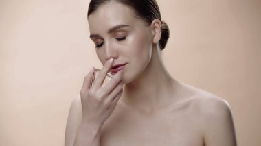 young woman with closed eyes smelling perfume isolated on beige