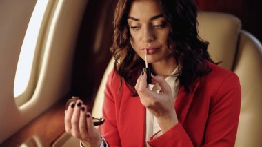 Businesswoman applying lip gloss in private airplane 