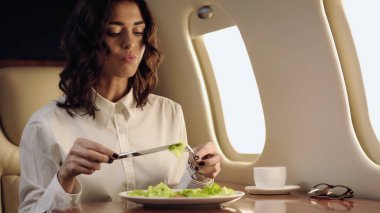 Businesswoman holding cutlery near blurred salad and coffee in private jet 