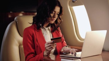 Businesswoman using laptop and holding credit card in private plane 