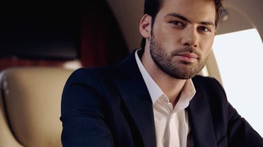 Bearded businessman in suit looking at camera in private jet 