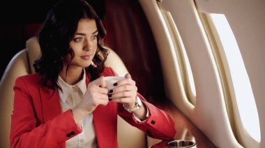 Businesswoman holding cup looking at window in private plane 