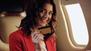 Cheerful businesswoman holding credit card in private plane 