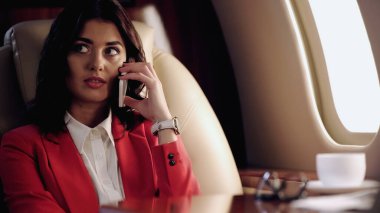 Businesswoman talking on cellphone near blurred cup in private plane 
