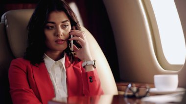 Upset businesswoman talking on smartphone near cup in private plane 