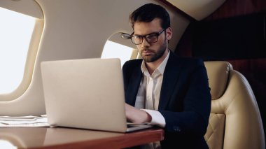 Businessman using blurred laptop near papers in private jet 