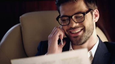 Smiling businessman talking on cellphone and reading newspaper in private jet 