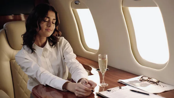 Young businesswoman sitting near champagne and newspaper in private plane