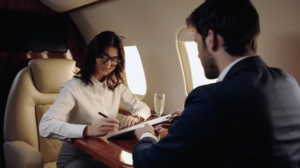 Businesswoman Writing Clipboard Champagne Colleague Private Plane — стоковое фото