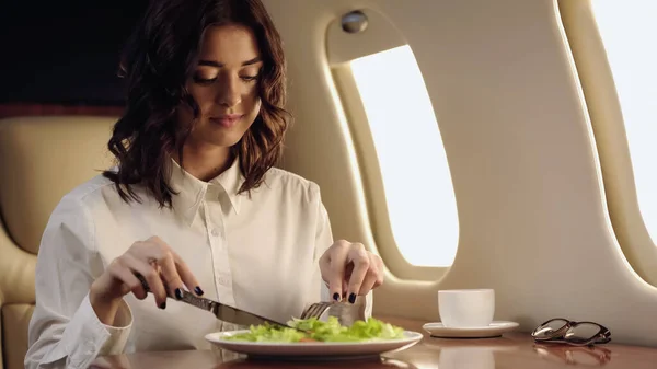 私人飞机上 年轻的女商人在沙拉和咖啡附近拿着餐具 — 图库照片