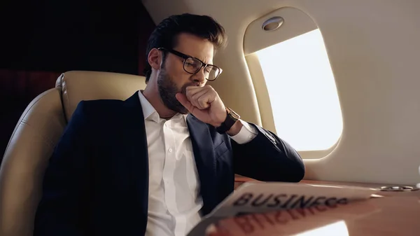 Businessman yawning near newspaper in private plane