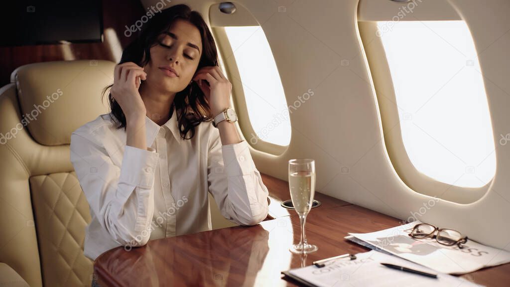 Businesswoman sitting near champagne and newspaper in private jet 