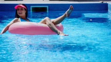 Çıplak ayaklı ve mutlu bir kadın havuzda şişme yüzükte yüzüyor.