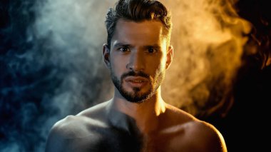 Portrait of bearded sportsman looking at camera with smoke on black