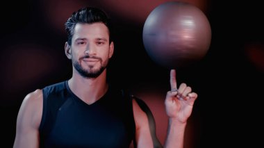 pleased young sportsman spinning blurred basketball on finger on black 