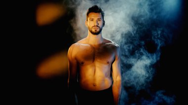 muscular sportsman looking at camera with smoke on black