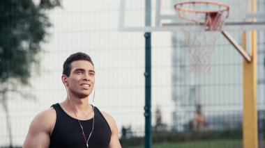 Kulaklıklı genç, melez bir sporcu. Bulanık basketbol sahasının yanından uzağa bakıyor.