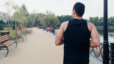 Kulaklıklı, çift ırklı atletik bir adamın arka görüntüsü.